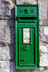 Oude groene brievenbus met tijdentabel ingemetseld in de muur van een gebouw. 