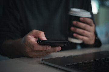Close-up of person using smartphone while holding coffee cup at desk