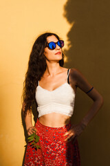 Fashionable young woman with curly hair in sunglasses posing confidently against a vibrant yellow wall on a bright summer day. © Nikola Spasenoski