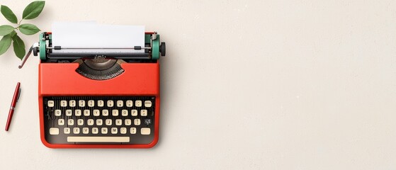 Vintage red typewriter with fresh green leaves on a neutral background.