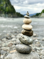 Round stones are set on top of each other against the background of a river and a mountain landscape. Altai, Russia. A conceptual symbol of natural balance.