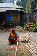 Rural woman working with bamboo sticks sitting in her yard 