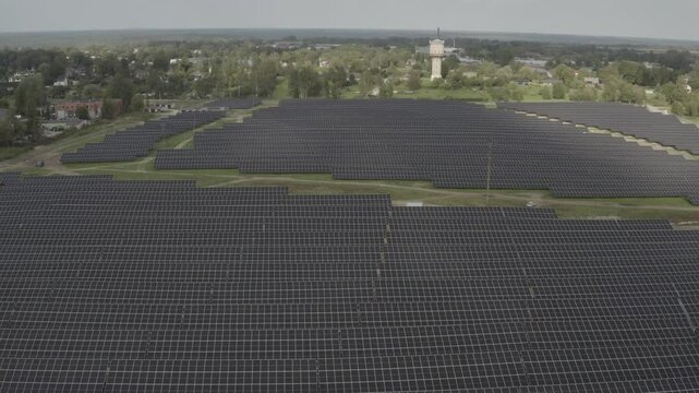 Aerial view of an expansive solar farm with rows of panels stretching across the landscape, near a town. Captured in high-quality s-log and 4K.