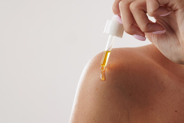woman applying oil and serum on body with pipette close-up, on white background