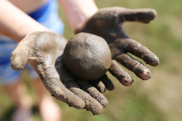 Child Playing Outside in Mud Holding Ball of Clay in Hands