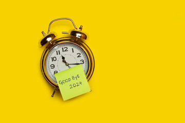 A bell alarm clock with a sticky note with goodbye 2024 short phrase written on it on a yellow...