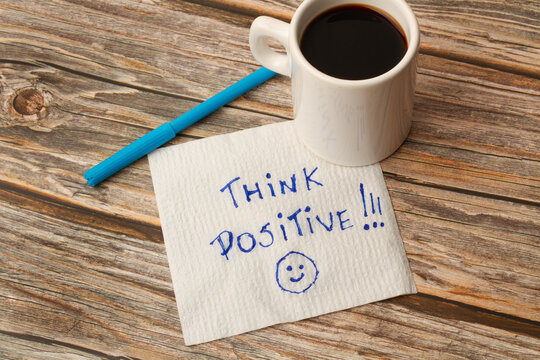 A mug with coffee on a paper with think positive short phrase and a marker on a wooden table