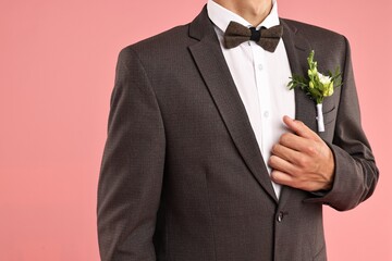 Groom in suit with stylish boutonniere on pink background, closeup
