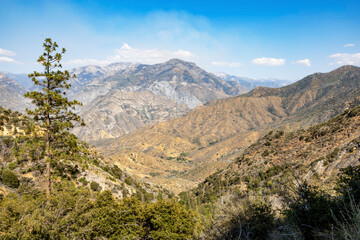 A stunning view of rugged mountains and valleys in King's Canyon National Park, California, captured during a scenic drive. The arid landscape and vast wilderness create a breathtaking scene.