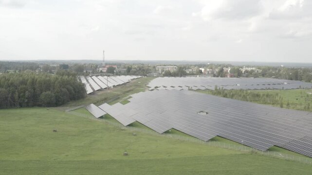Aerial view of a large solar farm near a town, featuring rows of solar panels across green fields. Captured in high-quality s-log and 4K.