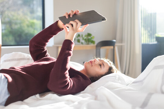 Relaxing in bed, woman holding tablet and reading, enjoying leisure time