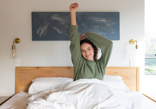 Stretching in bed, woman waking up and smiling, enjoying morning relaxation