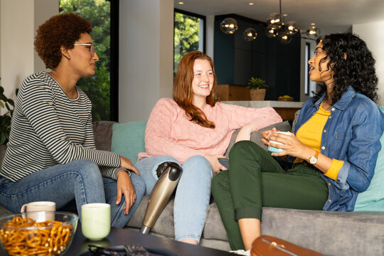 Chatting and relaxing on couch, diverse women friends enjoying coffee and snacks