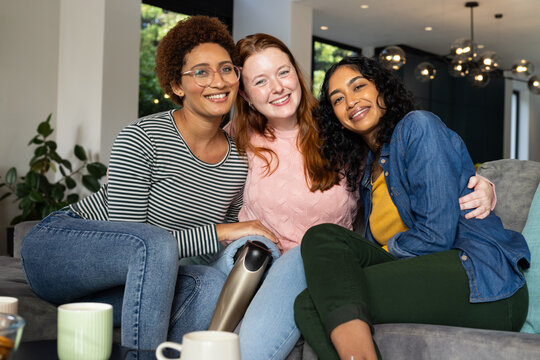 Smiling diverse women friends sitting on couch, enjoying coffee and spending time together