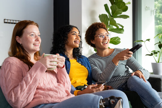 Watching TV, diverse group of women friends relaxing on couch with drinks