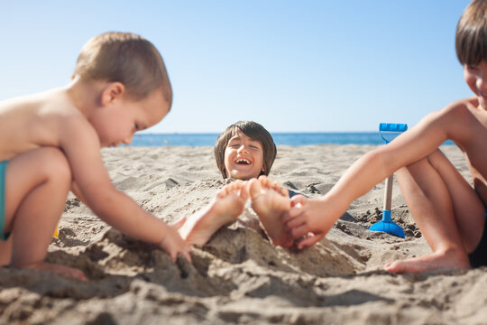 Child laughing when other children tickle his feet at the beach