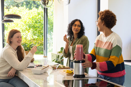 Making smoothies, diverse friends enjoying conversation in modern kitchen together - Powered by Adobe