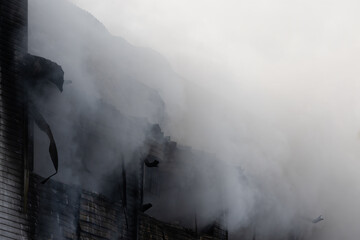 Hard gray plumes of smoke from an industrial fire on black wall warehouse background. Puffs of heavy smoke from broken windows