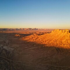 Soaring over a desert landscape at dawn, capturing the golden sands, dramatic dunes, and long shadows stretching across the barren ground