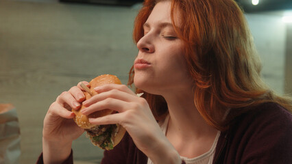 Young Caucasian woman female girl customer client eating junk fast food bite chewing burger...