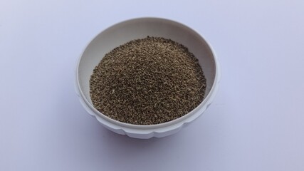 Closeup of carom seeds in bowl on white background
