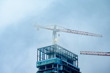 Fototapeta premium skyscraper construction site with crane lost in low cloud shot in toronto room for text
