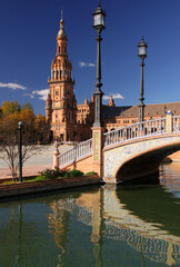 Photo with the view of Plaza de Espana with pavilion, water canal and bridge across it against a blue sky with clouds in Seville city, Andalusia region, southern Spain