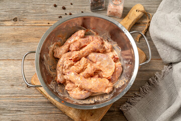 Raw chicken necks in a marinade in a bowl on a gray wooden culinary background. Top View