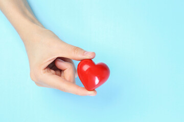 Woman holding red heart on light blue background, top view