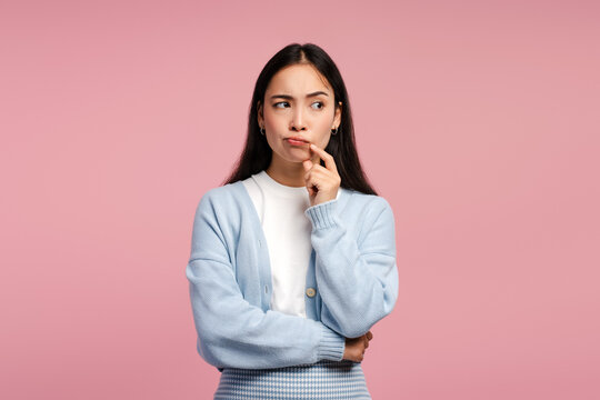 Young woman thinking hard keeping hand on chin posing on pink background, looking away