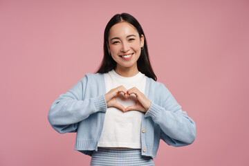 Smiling, beautiful woman making heart shape with hands standing isolated on pink background