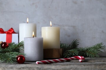 Burning candles, Christmas decor and fir tree branches on wooden table, closeup
