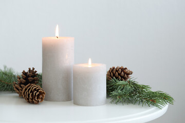 Burning candles and fir branches on coffee table near light wall, space for text. Christmas...