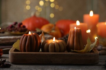 Burning candles in shape of pumpkins and autumn decor on wooden table