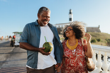 Happy senior couple enjoying a relaxed walk on holiday with a coconut drink