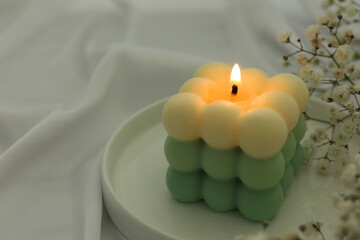 Stylish bubble candle and gypsophila flowers on white cloth, closeup. Space for text