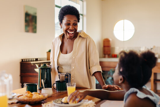 Happy Brazilian mother serving her daughter cheese bread rolls at breakfast