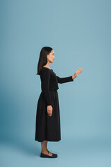 Beautiful, smiling Asian woman reaching for something on blue background