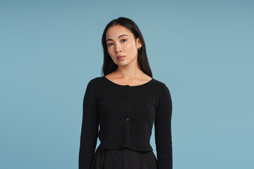 Serious young Asian woman wearing black casual clothes posing on blue background