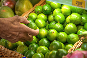 Mature man picks fresh lime fruit in supermarket close-up.
