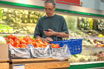 Mature man chooses yellow bell peppers in supermarket