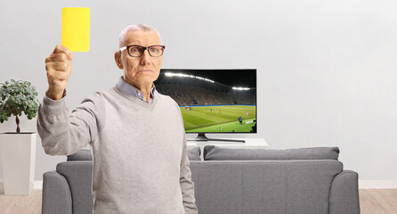 Serious elderly man showing a yellow card in front of tv screen