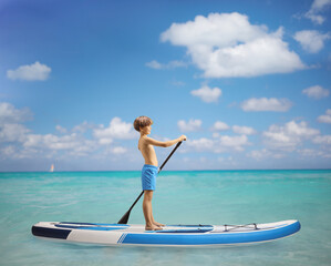 Full length profile shot of a boy standing on a SUP and paddling