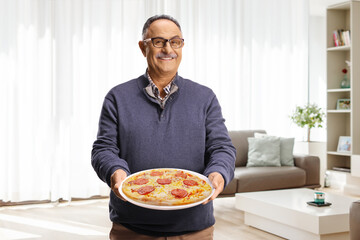 Mature man holding a pepperoni pizza on a plate at home