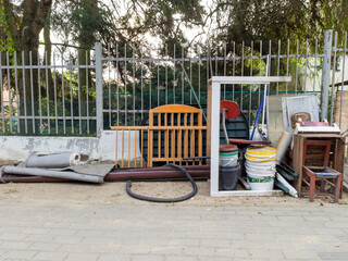 Various discarded items and furniture near a street fence