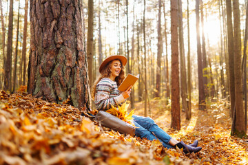 A woman reading a book while sitting on autumn leaves next to her bicycle in a serene forest during golden daylight hours