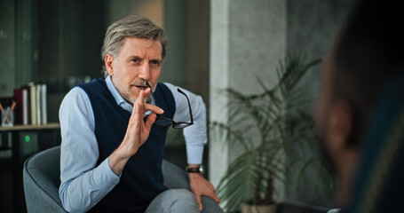 Mature psychologist sits in chair, asks questions, listens to patients on counseling session....