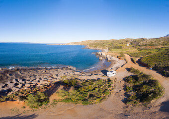 Fototapeta premium White camper van is parked near beach on a sunny day, offering a peaceful and scenic getaway. Peloponnese, Greece.
