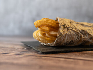 Churros wrapped in paper on slate and wooden background