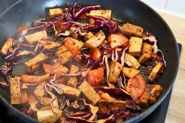 Colorful vegan stir fry with tofu, kale, cabbage, and carrots in a hot pan. A healthy and nutritious dish, full of vibrant vegetables and plant-based protein.